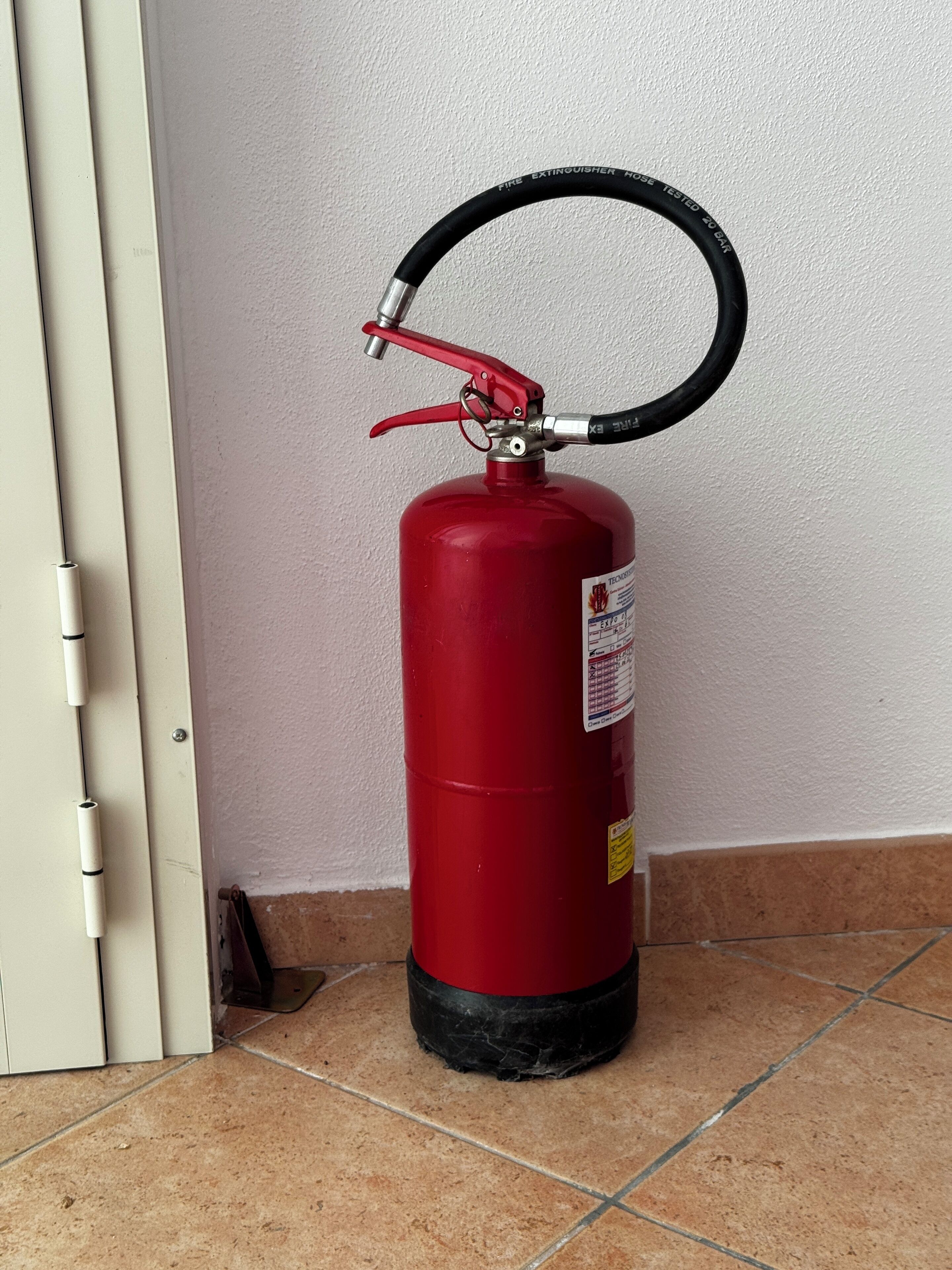 Ein roter Feuerlöscher ist an einer Wand neben einer Tür angebracht.