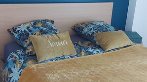 Ein Bett mit einem blumigen Überwurf und zwei Kissen, eines davon mit der Aufschrift "Amour".