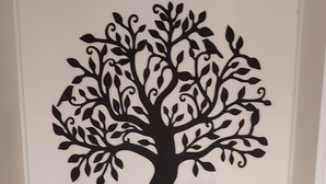 Ein türkisfarbenes Schränkchen mit zwei Türen, eine dekorative Baum-Abziehbild auf der darüberliegenden Wand, ein kleiner Topfpflanze, eine Kerze und eine goldene Spule Faden.