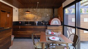 A modern kitchen with a stone wall, wooden cabinets, and a dining area with a table set for two. - Loft by the Lagoon: Bathtub with View & Nature (Florianópolis)