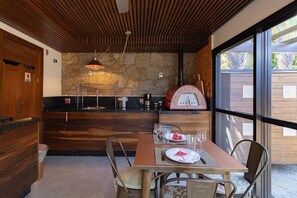 A modern kitchen with a stone wall, wooden cabinets, and a dining area with a table set for two. - Loft by the Lagoon: Bathtub with View & Nature (Florianópolis)