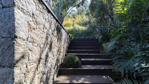 A stone wall adjacent to a wooden staircase surrounded by lush greenery. - Loft by the Lagoon: Bathtub with View & Nature (Florianópolis)