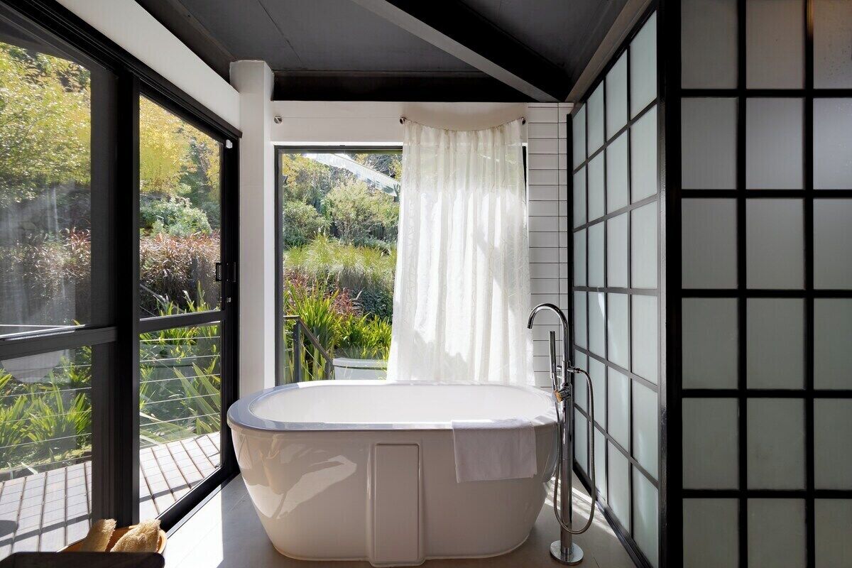 Een moderne badkamer met een vrijstaand bad, grote ramen en uitzicht op groen.