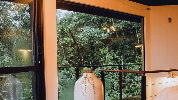 A room with large windows, a wooden table with two cups and a teapot, and a view of greenery outside. - Loft by the Lagoon: Bathtub with View & Nature (Florianópolis)