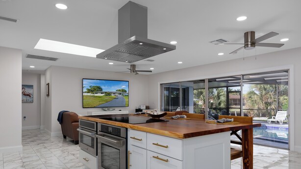 A modern kitchen with a large island, built-in oven, and a view of a swimming pool. - Waterfront Canal Home with Private Pool . Family Getaway . New Rental (Cape Coral)