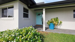 A house with a light-colored exterior, a blue door, and a large potted plant on the porch. - Waterfront Canal Home with Private Pool . Family Getaway . New Rental (Cape Coral)