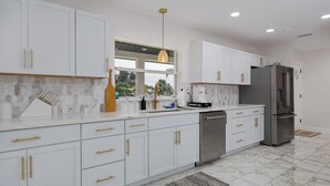 A modern kitchen with white cabinets, stainless steel appliances, and a large window. - Waterfront Canal Home with Private Pool . Family Getaway . New Rental (Cape Coral)
