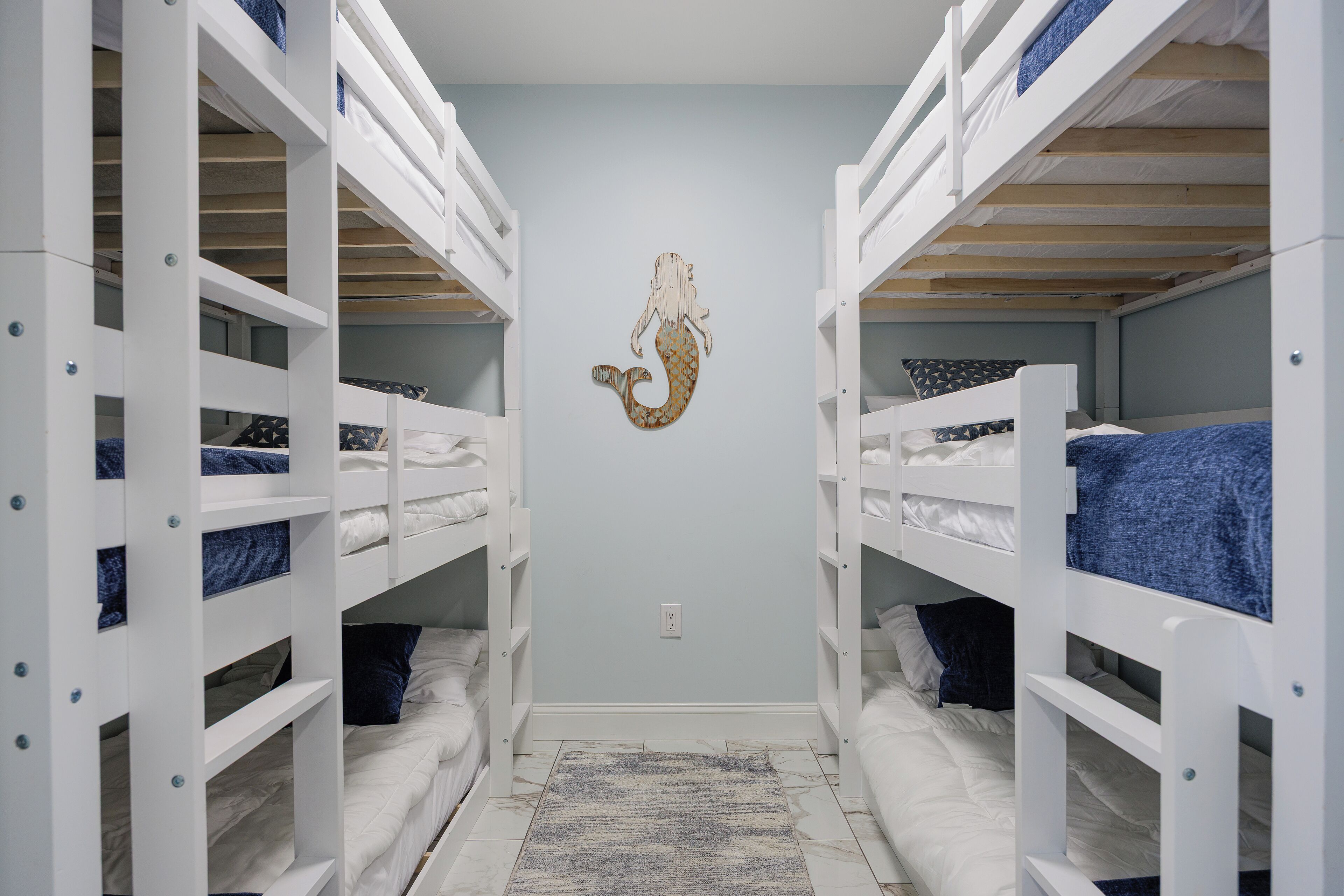 Una habitación con literas, pared azul claro y decoración con sirenas.