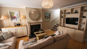 Una sala de estar con sofá, mesa de centro, chimenea, televisor y escalera.