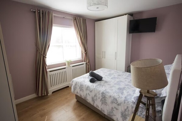 A bedroom with a bed, a radiator, a TV, and a lamp.