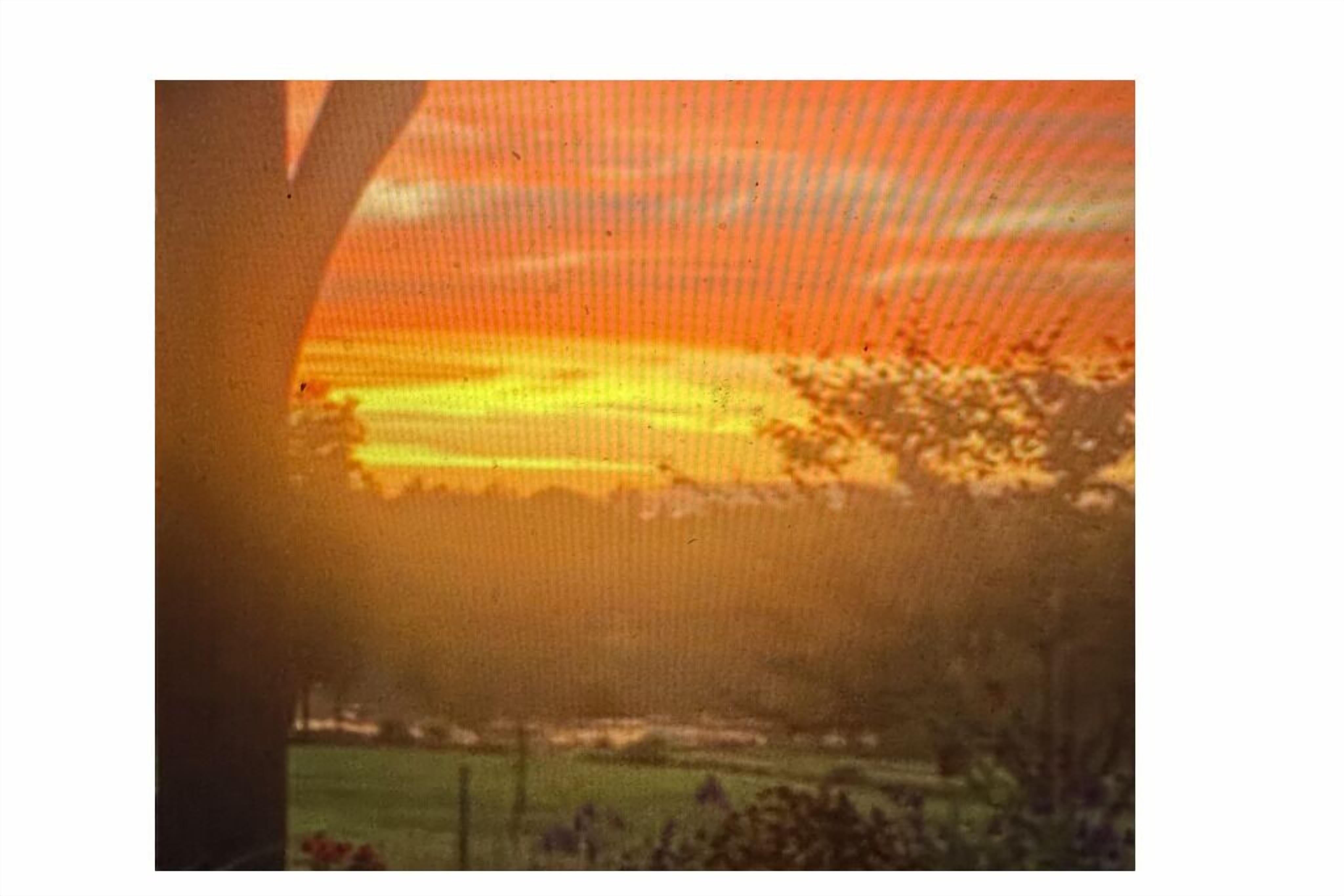 A sunset view through a window with a fence in the foreground.