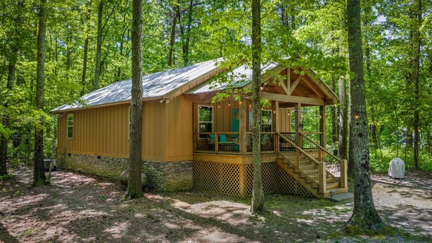 Une cabane en bois avec un porche et un escalier, entourée d’arbres.