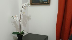 Una habitación de hotel con una cama, un escritorio con una orquídea en maceta, una silla de oficina negra, una cortina roja y un cuadro en la pared.