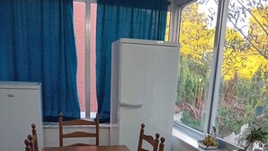 Un comedor con una mesa y sillas de madera, un refrigerador blanco y una ventana con cortinas.