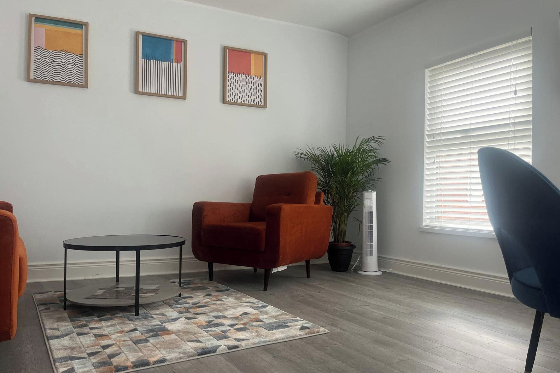 A living room with a round table, two armchairs, a potted plant, and a window with blinds.