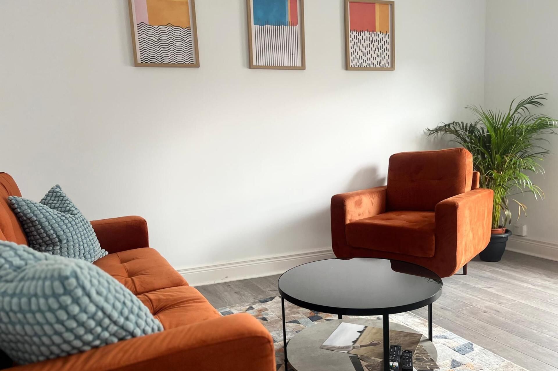 A living room with an orange sofa, a round coffee table, and three framed abstract artworks on the wall.