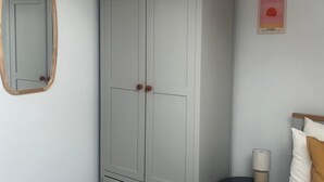A bedroom with a grey wardrobe, a bedside table with a lamp, and a poster on the wall. - 2 Bed Apartment Sleeps 4 - Free Parking (Belfast)