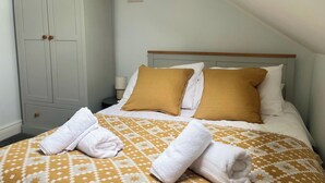 A neatly made bed with a patterned bedspread, two pillows, and two rolled towels on a white wall with a poster. - 2 Bed Apartment Sleeps 4 - Free Parking (Belfast)