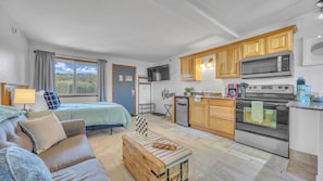 Une pièce de taille modeste comprenant un lit, un canapé, une commode en bois, un coin cuisine et un téléviseur.