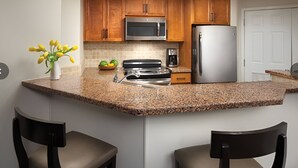 Eine Küche mit Granit Arbeitsplatten, Holzschränken, einem Edelstahlkühlschrank, einer Mikrowelle und einem Herd.