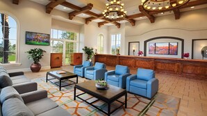 Eine großzügige Lobby mit einer Rezeption, blauen Sesseln, einem Sofa und einem Couchtisch.