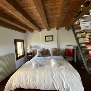 A bedroom with a wooden ceiling, a bed with white linens, a bedside table with a lamp, a radiator, a window, and a bookshelf. - Sandstone Home in the Heart of the Prosecco Hills, between Venice and Cortina. (Borgo Antiga)