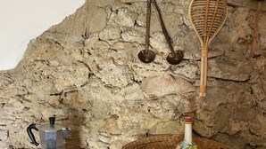 Une cuisine avec un mur en pierre, une machine à café, un panier en osier contenant une bouteille décorative et des ustensiles suspendus.