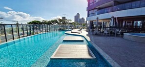A rooftop swimming pool with clear blue water, surrounded by a glass railing and a modern building in the background. - COJAG0103 - Beach Class Jaguaribe (Salvador)