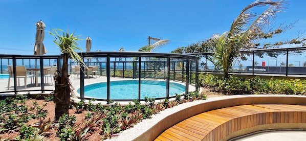 Un espace piscine doté d’une structure en verre, entouré de plantes et de bancs en bois.