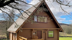 Une cabane en bois avec un toit en pente, une véranda en bois et une allée gravillonnée.