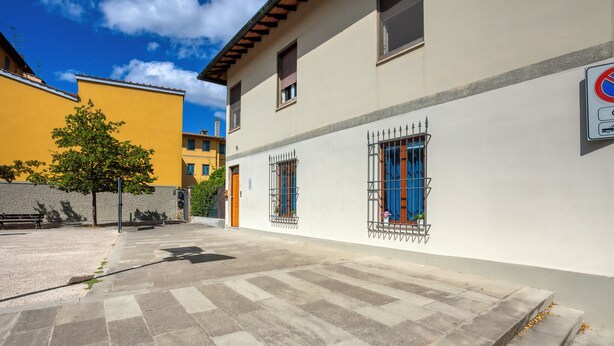 En innergård med stenbeläggning, ett träd och en byggnad med gallerförsedda fönster och en skylt som förbjuder parkering.