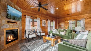 Ein gemütliches Blockhaus-Interieur mit Kamin aus Stein, Holzbalkendecke und einem grünen Sofa.
