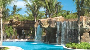 A resort pool with a waterfall feature, surrounded by palm trees and lounge chairs. - Cozy 2-bedroom condo with AC in charming Bonita Springs (Bonita Springs)