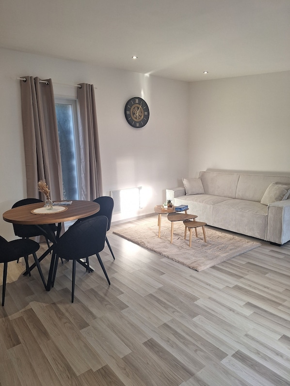 Un salon moderne avec une table à manger en bois, des chaises noires, un canapé beige et une petite table basse.
