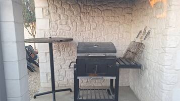 A barbecue grill with a stone wall backdrop, a small table, and a grill cover.