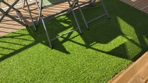 Un patio con una mesa de vidrio y dos sillas, rodeado por una cerca de madera y vistas a casas al fondo.