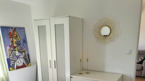 Un dormitorio con cama, armario, escritorio y espejo adosado a la pared.