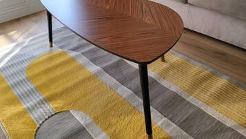 Un salon moderne avec une table basse en bois, un tapis à motifs rayés et un canapé gris agrémenté d’un coussin coloré.