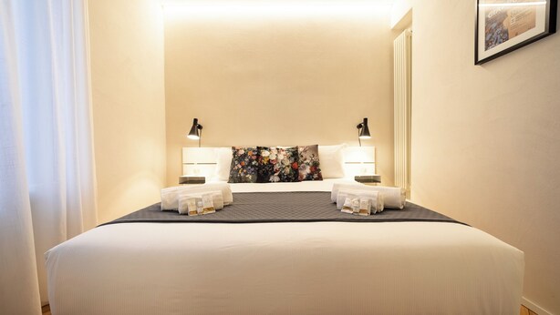 Una cama bien hecha con sábanas blancas, dos lámparas de noche y una obra de arte floral en la cabecera.