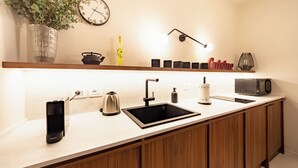 Una cocina moderna con un lavamanos integrado, una tetera, una cafetera, un microondas y una estantería con utensilios de cocina.