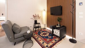 Una sala de estar moderna con un sofá gris, una mesa redonda de centro, un tapete estampado, una mesita auxiliar negra con un florero, una lámpara de pie negra y un televisor montado en una pared de madera.