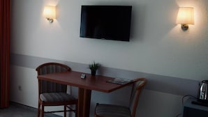 A hotel room with a flat-screen TV mounted on the wall, two wall-mounted lamps, a wooden table with two chairs, a small potted plant, and a coffee maker on a side table. - Gästehaus Tilly Hotel (Hann. Muenden)