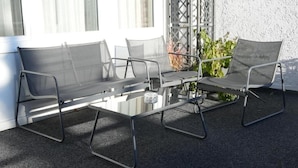 A modern outdoor seating area with a glass-top table and metal chairs. - Gästehaus Tilly Hotel (Hann. Muenden)