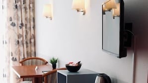 A hotel room with a wooden dining table, two chairs, a small potted plant, a bowl of fruit, a kettle, and a mirror on the wall. - Gästehaus Tilly Hotel (Hann. Muenden)