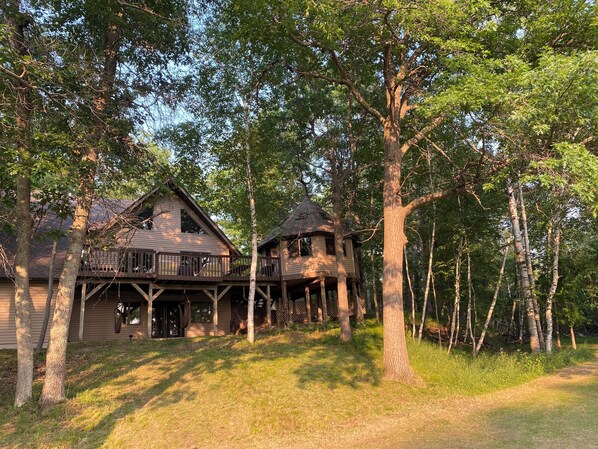 A cabin with a wooden deck and a separate tower-like structure, surrounded by trees.
