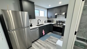 A modern kitchen with stainless steel appliances, dark cabinetry, and a window providing natural light. - The Secure Haven (Regina)