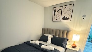 A neatly made bed with a dark blue comforter and white pillows, a bedside lamp, and a fluffy rug. - The Secure Haven (Regina)