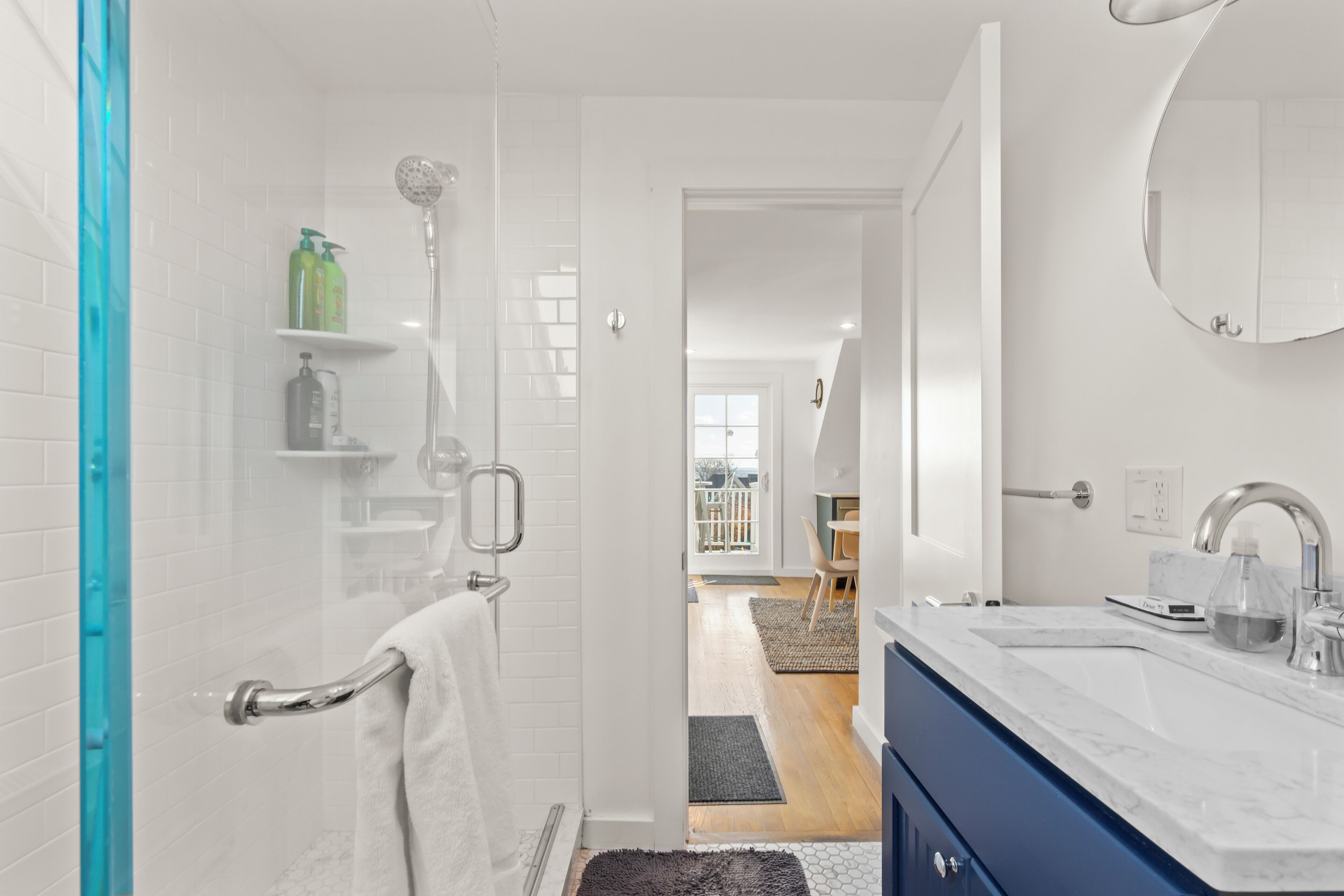A modern bathroom with a shower, a sink, and a mirror. There is a towel rack and a glass shower door.