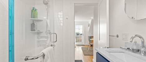 A modern bathroom with a shower, a sink, and a mirror. There is a towel rack and a glass shower door.