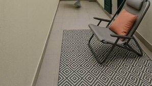 Kapea ulkoilmakäytävä, jossa on kuvioitu matto, tuoli, kierreportaat ja vihreä seinä, johon on ripustettu valonauha.